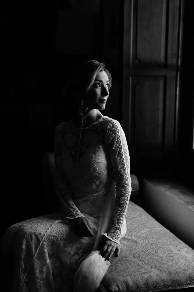 Bride in a lace dress sitting by a window in soft light, black and white